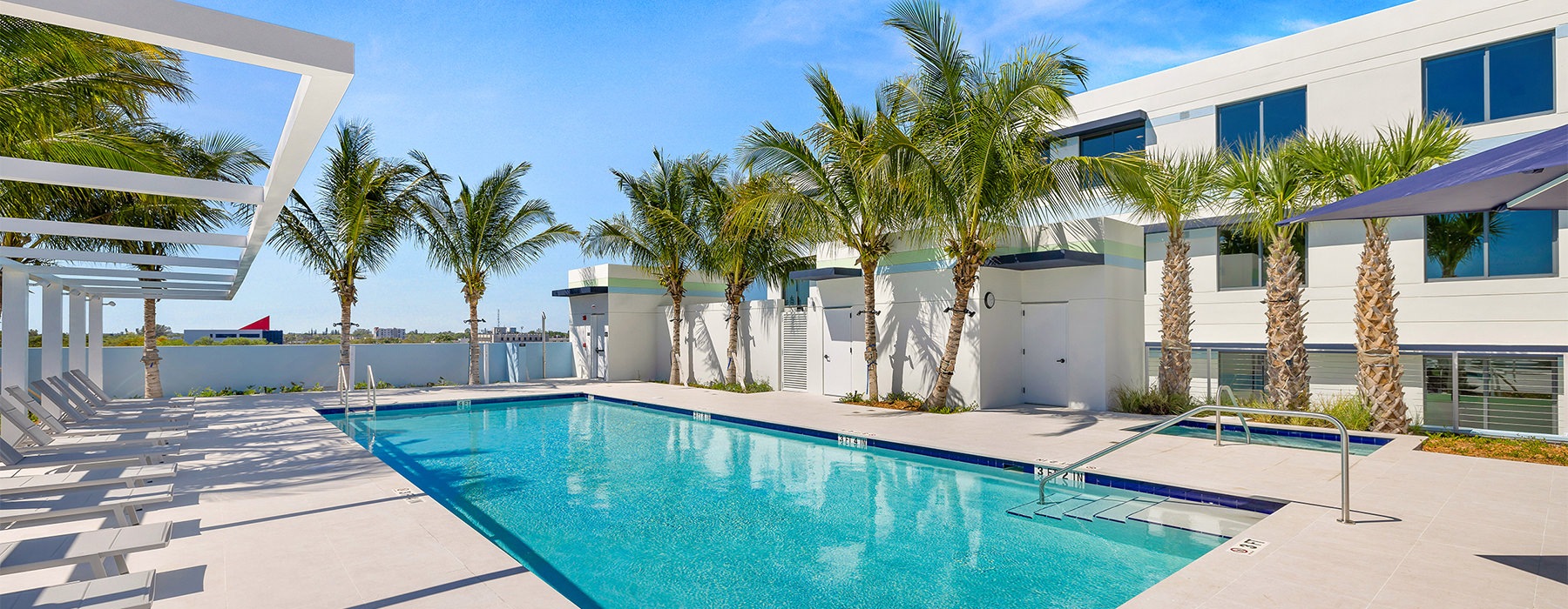 The pool area at Residences at Nomi apartments for rent in North Miami, FL, featuring lounge chairs and umbrellas.